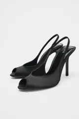 Zapato de tacón destalonado color negro con efecto satinado, punta fina, abertura delantera y tira trasera elástica. Tacón alto fino.