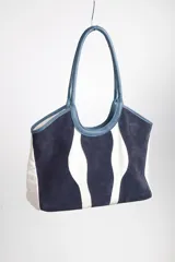 Bolso tipo tote de cuero y gamuza azul con diseño de ondas blancas. Tiene doble asa de cuero azul y base de cuero graneado. El exterior es de gamuza y tela 100% algodón.