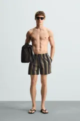 Bañador corto de tejido técnico con rayas verticales en tonos negro, verde oliva y rosa. Cuenta con cintura elástica ajustable con cordón, bolsillos laterales y trasero.