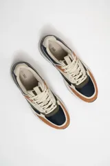 Zapatillas deportivas acordonadas con capellada de cuero sintético color beige, detalles en azul marino, verde oliva y marrón. Suela blanca con base negra.