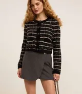 Minifalda gris de tweed con diseño cruzado, cierre lateral con cremallera oculta y dos botones dorados decorativos en la parte delantera.