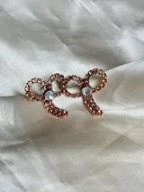 Par de aros colgantes con forma de moño, con engarce de strass color oro rosa y detalle de cristal facetado.