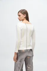 Remera blanca de corte recto y escote barco, con mangas largas y bordado de líneas verticales en color gris y amarillo.