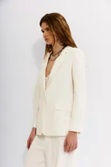 Blazer color blanco hueso, con solapas de muesca, cierre frontal con un botón y bolsillos delanteros con solapa.