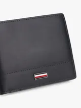 Billetera plegable de cuero negro con logo de Tommy Hilfiger esmaltado en la parte delantera. Cuenta con múltiples ranuras interiores para tarjetas, compartimento para billetes y bolsillo para monedas.