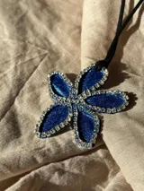Collar con dije de flor azul brillante con borde de strass plateado y cordón negro.