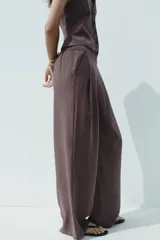 Pantalón palazzo color marrón topo, de tejido fluido, tiro medio, cintura elástica, bolsillos laterales y pinzas frontales.