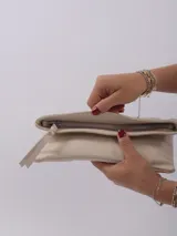 Sobre de mano color crema, con cierre de cremallera y tira de cuero para sujetar a la muñeca.