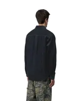 Camisa de manga larga confeccionada en pana de color azul marino, con cuello clásico y cierre frontal de botones. Presenta un bolsillo de parche en el pecho con la etiqueta de la marca Carhartt.