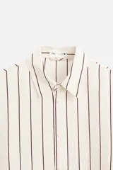 Camisa de hombre regular fit, color blanco con rayas verticales negras, cuello solapa, manga larga con puños abotonados y cierre frontal con botones.