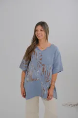 Blusa celeste con estampado de hojas marrones, cuello en V con terminación desflecada y mangas cortas.
