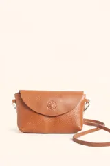 Cartera tipo bandolera de cuero vacuno color suela, con solapa frontal, cierre principal y broche. Presenta un diseño minimalista con un detalle de flor grabado en la solapa y correa larga ajustable.