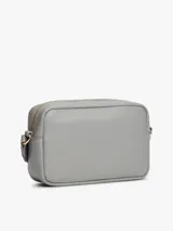 Cartera bandolera rectangular de cuero sintético color gris claro, con cierre superior de cremallera y logo metálico de Tommy Hilfiger en el frente.