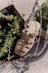 Sandalias de cuero marrón con diseño de tiras entretejidas y hebilla lateral.