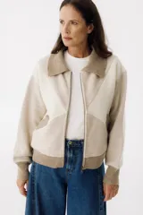 Campera bomber color beige con bloques de color en crudo y marrón claro. Tiene cuello clásico, cierre frontal con cremallera, bolsillos laterales y puños y ruedo acanalados.
