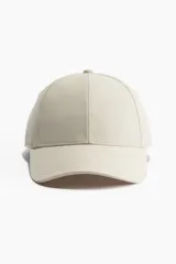 Gorra deportiva color beige, de tejido funcional repelente al agua, con cinta antitranspirante y trabilla ajustable con cierre de metal en la parte posterior.