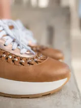 Zapatillas deportivas urbanas de cuero vacuno color blanco con detalles en cuero color beige y trenzado artesanal.