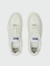 Zapatillas Diesel modelo S-Oval Skate, color blanco hueso o crema, de corte bajo y estilo skate. Presentan paneles superpuestos, forro interior de felpa y suela gruesa con textura. El logo DIESEL es visible en la lengüeta y un dije metálico con logo adorna los cordones.