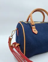 Cartera tipo bowling de jeans azul con detalles en cuero sintético color camel. Incluye llavero de peluche y dije de flor.