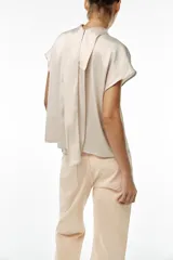 Blusa color crudo de tejido satinado, con cuello subido, manga sisa y cierre en la espalda con lazada y botones.