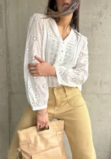 Camisa blanca de algodón con bordado inglés, cuello en V y mangas largas abullonadas.