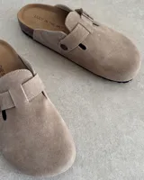 Zuecos marrones de gamuza con hebilla metálica ajustable.