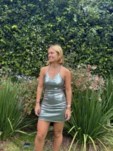 Vestido corto ajustado color plateado metalizado, con escote en V y tirantes finos que se cruzan en la espalda semi baja.