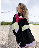 Buzo negro con bloques de color fucsia, verde y lila, con cuello alto con cierre y botones a presión.