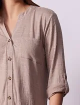 Blusa blanca texturizada marca Ninety, con cuello a la base, escote en V, abertura central con botones, bolsillo delantero y mangas tres cuartos regulables con presilla y botón.