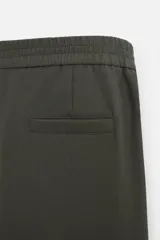 Pantalón largo color verde oscuro, de corte recto y tiro medio. Confeccionado en tejido con viscosa, con cintura elástica, bolsillos laterales y trasero de vivo. Cierre frontal con cremallera y botón.