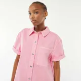 Mono corto color rosa de jean con cuello camisero, cierre frontal con automáticos metálicos, mangas cortas con dobladillo y bolsillos laterales.