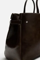 Bolso de mano extragrande color marrón oscuro, fabricado en piel de alta calidad. Tiene un compartimento principal con cierre magnético, un bolsillo interior con cremallera y un bolsillo secundario con solapa y cinta. Las asas son de piel.