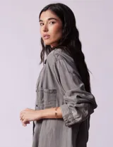 Camisa de jean celeste, marca Hester & Orchand, de corte oversize con cuello con solapa, escote en V y abertura central con botones. Delantera con bolsillos aplicados, mangas largas regulables con presilla y botón, y ruedo desflecado.