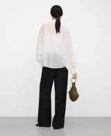 Camisa blanca de manga larga, con cuello chimenea alto y botonadura frontal oculta. El tejido es semitransparente y presenta una textura ligera.