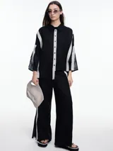 Camisa de lino color negro con silueta amplia y mangas 3/4. Diseño con tiras de color blanco en contraste en la cartera, mangas y cuerpo. Tiene tajos laterales y ruedo irregular en el frente.