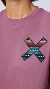 Remera manga corta color lila con cuello redondo y estampado en el pecho con forma de equis (X) con motivos geométricos en colores.