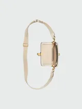 Bolso bandolera Marc Jacobs The Mini, color crema, con correa ancha de tela con logo de la marca y cadena dorada decorativa.