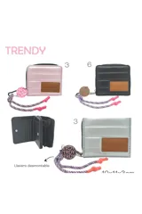 Billetera pequeña acolchada color rosa pálido metalizado, con cierre de cremallera. Presenta un parche de cuero marrón con texto grabado y un accesorio colgante con cordón estampado en tonos rosa y azul marino.