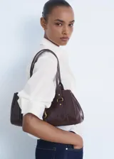 Camisa blanca de popelín de algodón, manga tres cuartos, corte crop y diseño recto. Presenta cuello camisero, bolsillo en el pecho con detalle de strass y cierre frontal con botones.