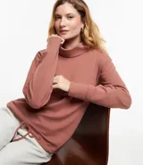 Polera hecha en tela canalé con tacto peluche, color ladrillo, con cuello alto, mangas largas y lazo en el bajo.