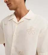 Camisa de hombre con corte boxy, cuello inglés y abotonado delantero. Es de color crema y presenta bordados sutiles de motivos veraniegos en tono naranja claro.