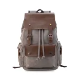 Mochila gris de tela canvas con detalles en símil cuero marrón. Tiene cierre superior marinero, bolsillos internos y externos con cierre metálico, asas rígidas y correas ajustables.