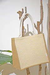 Bolso tipo tote de yute con rayas horizontales color beige y manijas de soga blanca.
