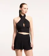 Blusa cropped de crepé color negro, con escote halter cruzado y espalda descubierta. Cierre lateral con cremallera y botones en el cuello.