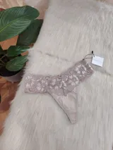 Bombacha tipo tanga color beige con encaje floral en la parte superior.