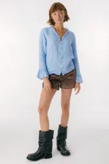 Blusa blanca de lino con botones de nácar, volados en el escote y mangas largas con puños acampanados. Corte recto y holgado.