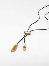 Collar con cordón negro ajustable y dije dorado con forma abstracta.