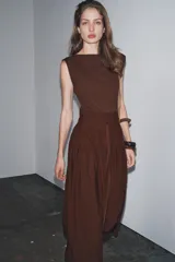 Vestido midi marrón con cuello barco y manga sisa. Presenta un corte a la altura de la cintura con detalle de trabilla y lazo del mismo tejido. Cierre lateral con cremallera oculta.