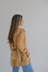 Blusa color ocre con estampado abstracto en tonos marrones y grises. Tiene cuello redondo y mangas 3/4 con botón.
