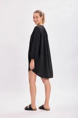 Vestido corto negro con cuello mao, abotonadura parcial y mangas largas abullonadas.